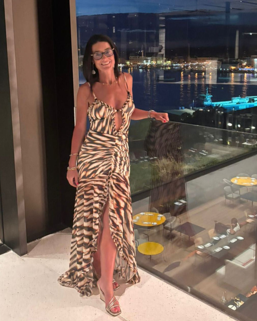 Woman in a zebra print dress standing on a balcony with a cityscape view at night.
